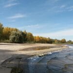 Plaża po sezonie: dlaczego warto przyjechać do Sztutowa jesienią Jesienna, pusta plaża nad wodą otoczona kolorowymi drzewami