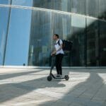 Sztutowo i okolice na hulajnodze: gdzie wolno, gdzie uważać, jak dojechać Mężczyzna na elektrycznej hulajnodze z plecakiem przed szklanym biurowcem