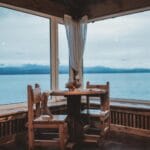 Gdzie najlepiej nocować w Sztutowie, jeśli chcesz codziennie jeździć do Krynicy Morskiej i wracać na spokojną bazę Przytulny pokój z drewnianym stołem i widokiem na jezioro oraz góry