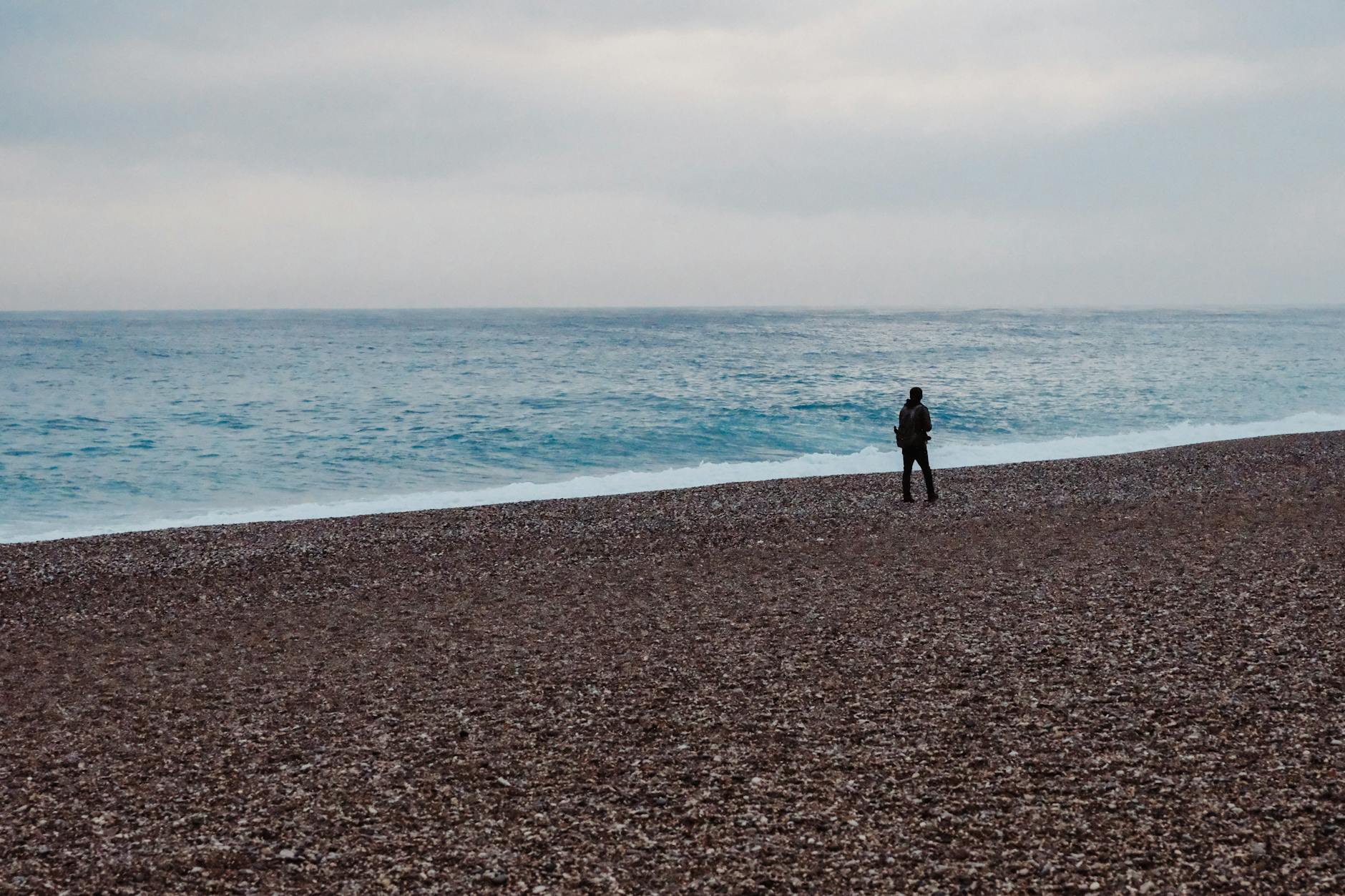 Plaża w Sztutowie bez parawanów: gdzie ludzie siedzą luźniej i spokojniej Pusta kamienista plaża z pojedynczą osobą nad morzem pod zachmurzonym niebem