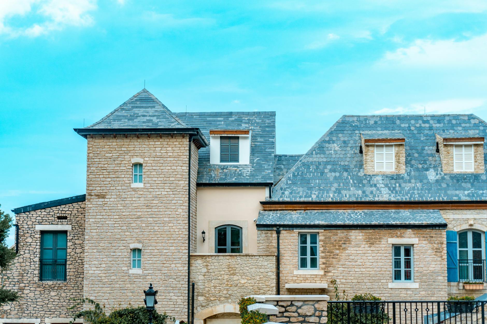 Jak wybrać kamień elewacyjny do domu jednorodzinnego – praktyczny poradnik inwestora Kamienny dom z szarym dachem z łupka i niebieskimi okiennicami