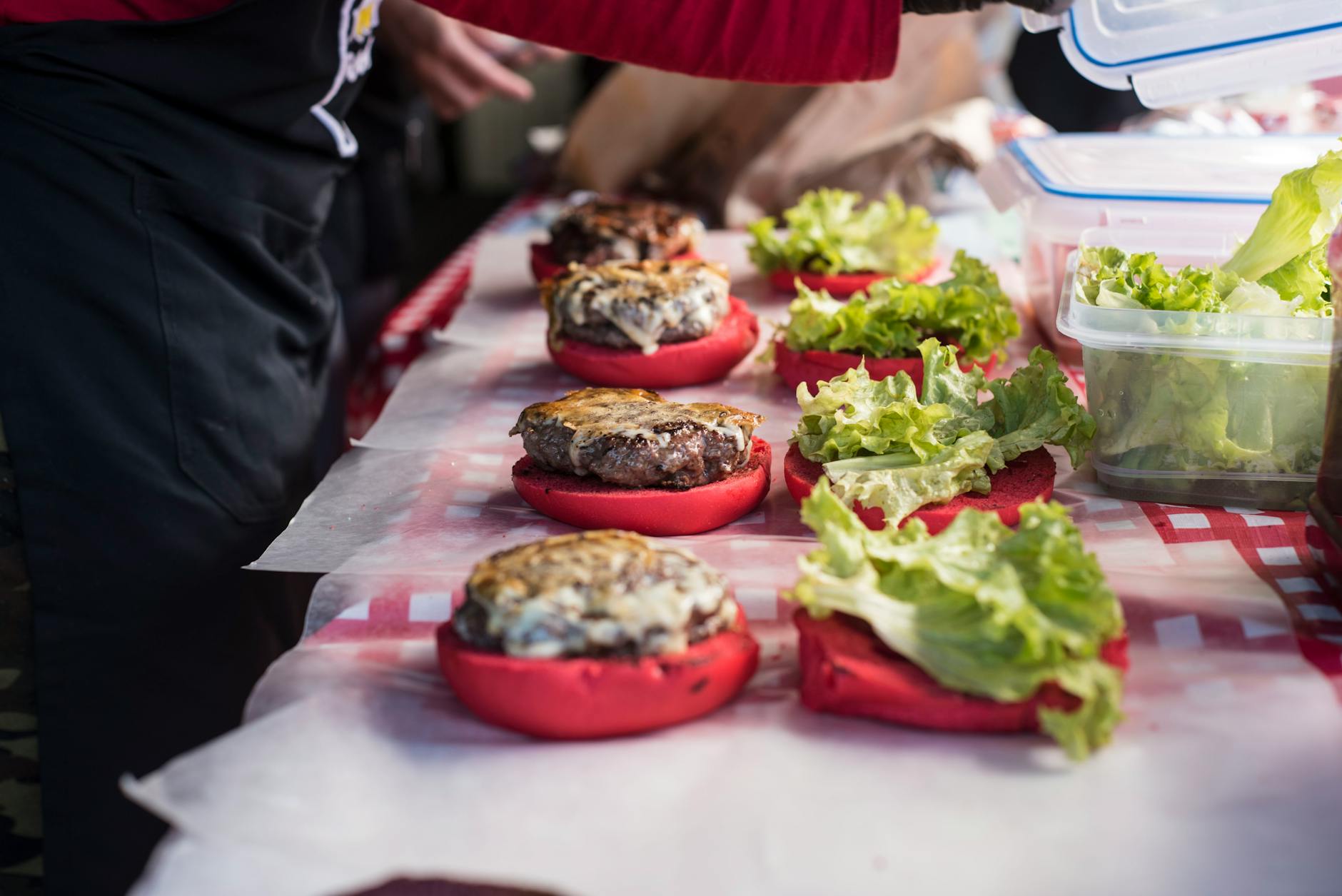 Gourmet burgery z czerwonymi bułkami przygotowywane na kraciastym stole