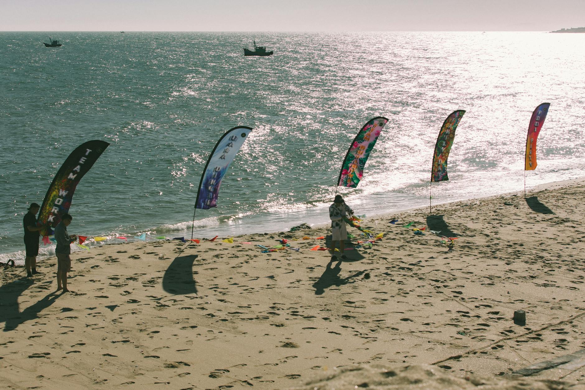 Kolorowe flagi na słonecznej plaży nad morzem, ludzie bawią się latem