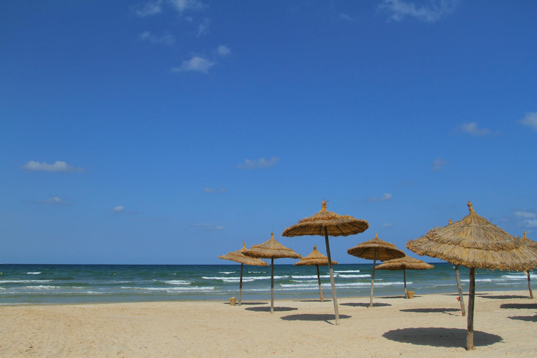 Najpiękniejsze plaże Tunezji – przewodnik po miejscach idealnych na pierwszy wyjazd Tunezyjska plaża z parasolami trzcinowymi w słoneczny, bezchmurny dzień