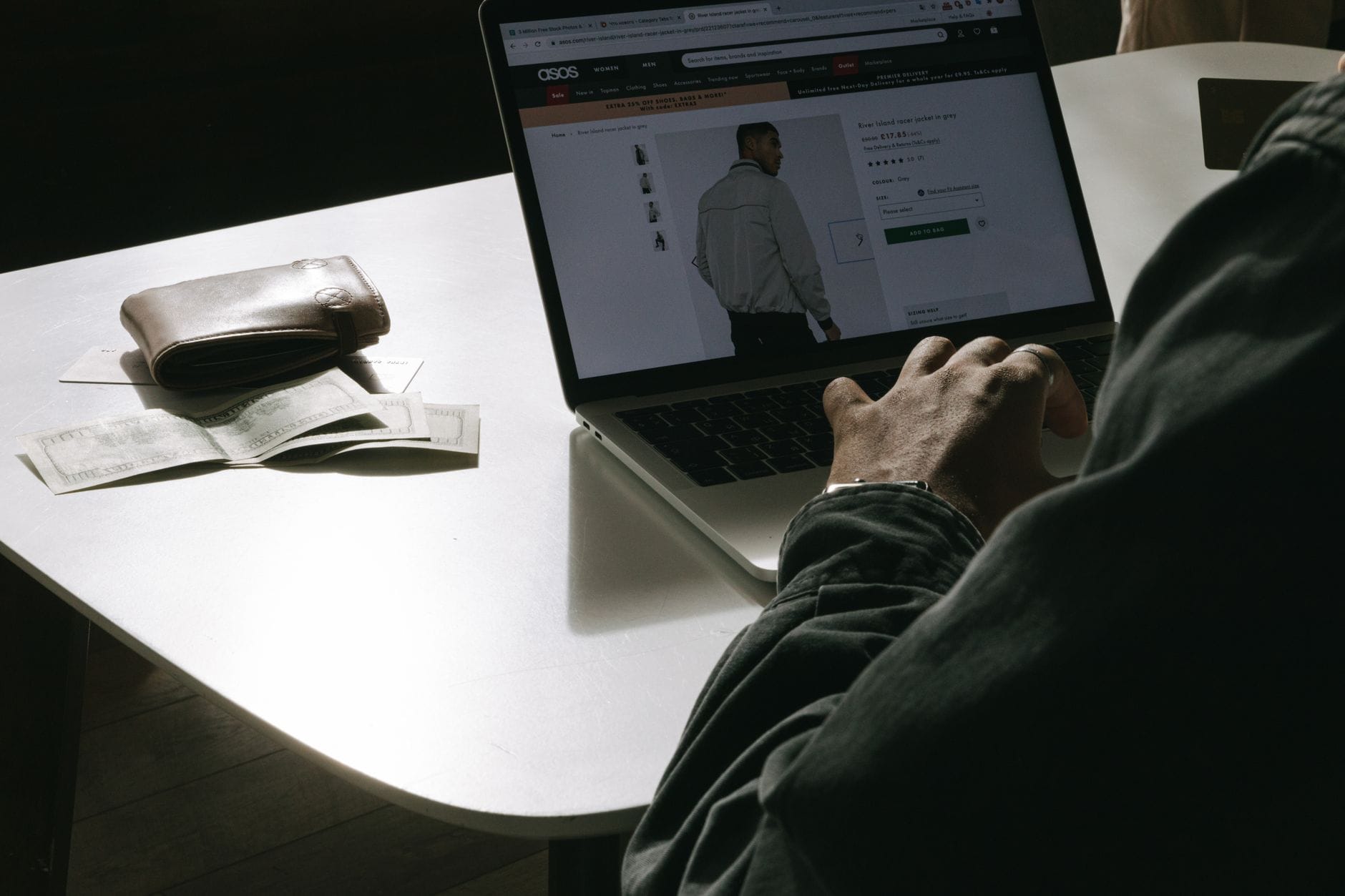 Mężczyzna w domu robi zakupy odzieży online na laptopie obok portfela