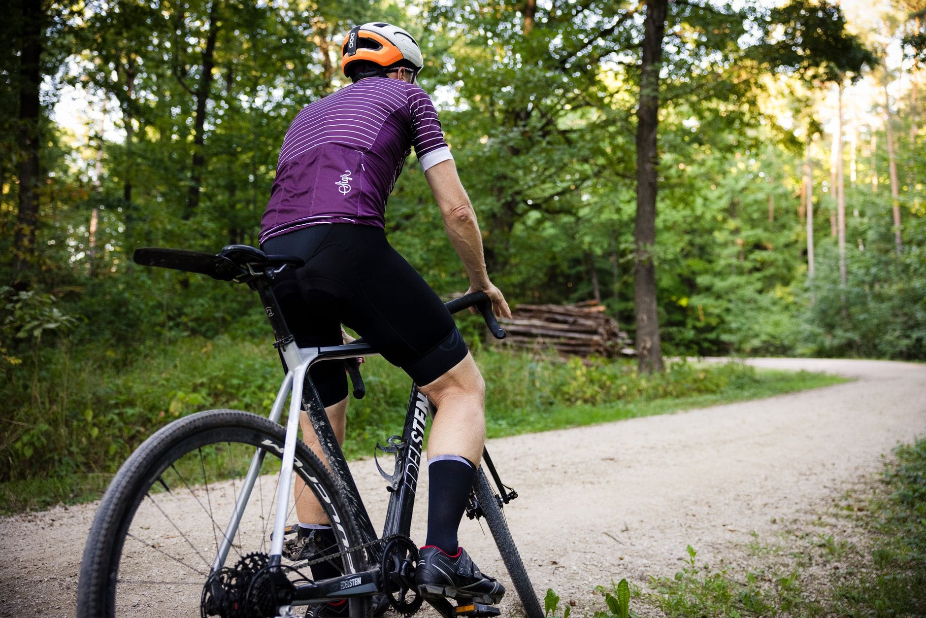 Rowerzysta w kasku jedzie leśnym szutrowym szlakiem w zielonym lesie